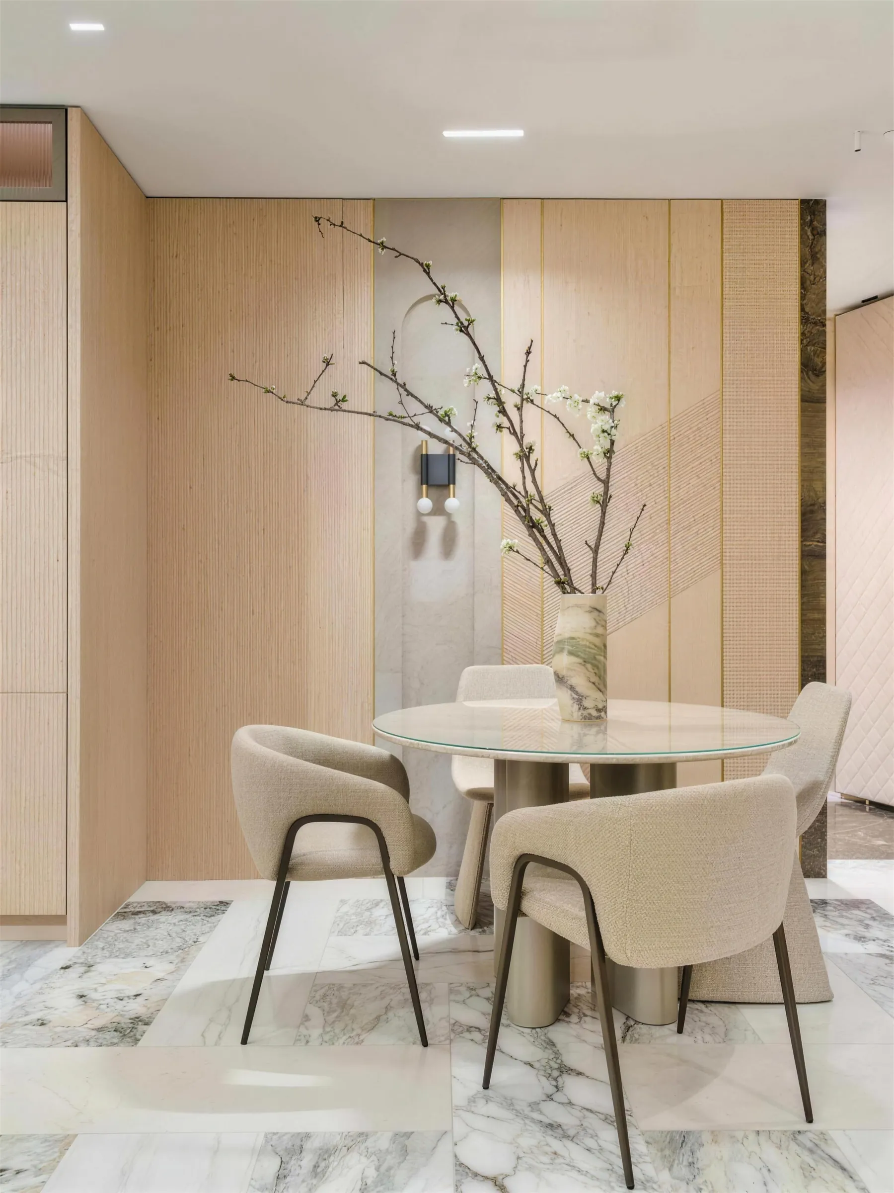 Dining area in the Faura showroom with a round table, bouclé chairs and blossom branches against oak and marble